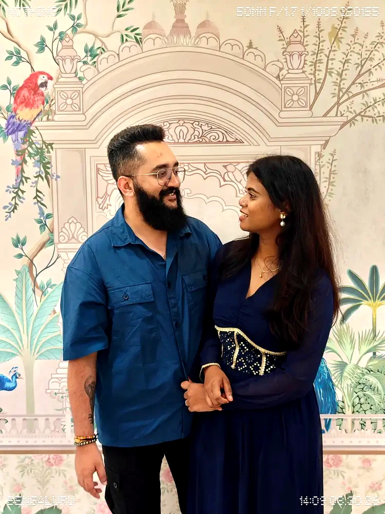 Mamtha and Prem in blue outfits in front of a colourful mural